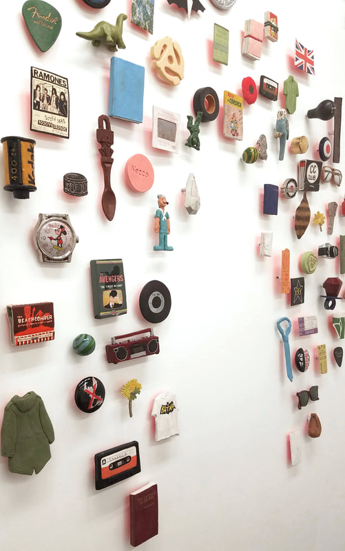 colorful array of objects on a white wall, arranged in a circle with a space for an absent figure