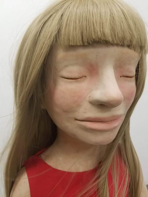 close of face of clay figure of a girl with closed eyes and dirty blond wig with short bangs