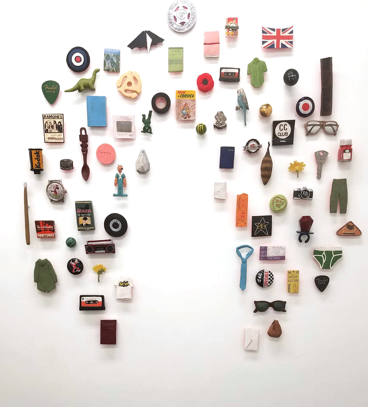 colorful array of objects on a white wall, arranged in a circle with a space for an absent figure