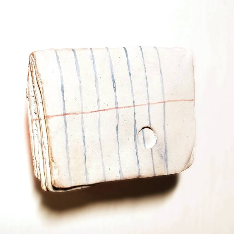 clay sculpture of a folded loose leaf note on a white wall